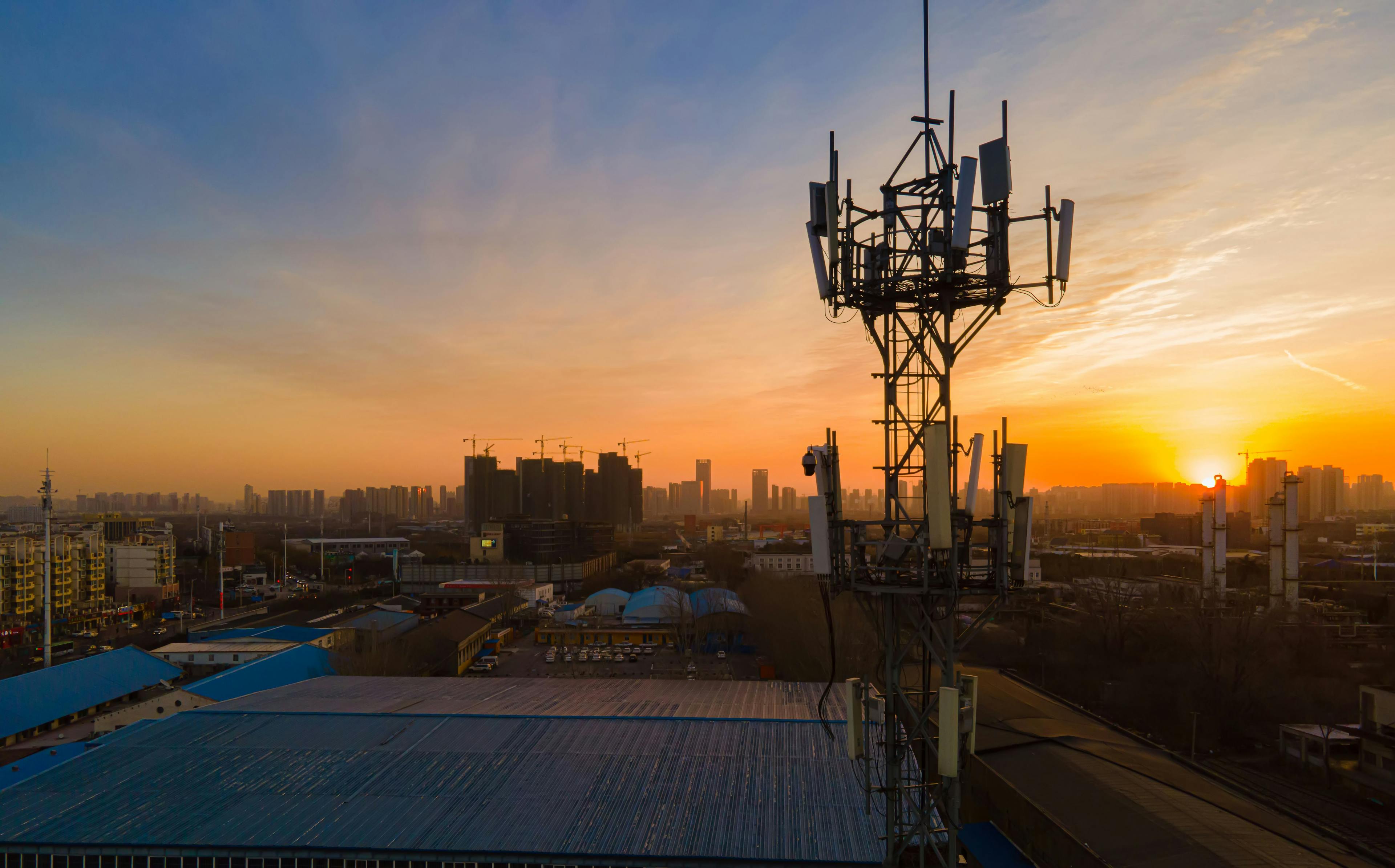 Image of a 5G tower with a city skyline and sunset in the background