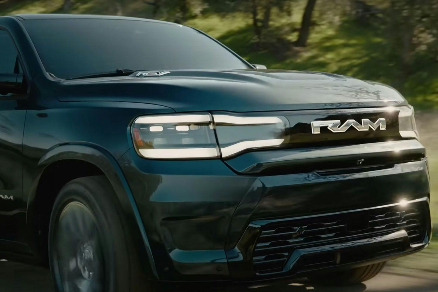 the front grill of a a black Ram 1500 REV drives on a road in a green wooded landscape